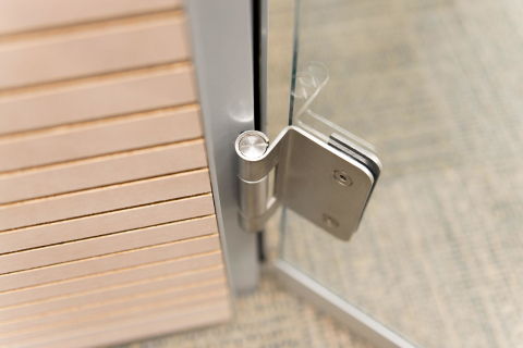 Detail of a stainless steel hinge of a DK42 door frame and a tampered glass door